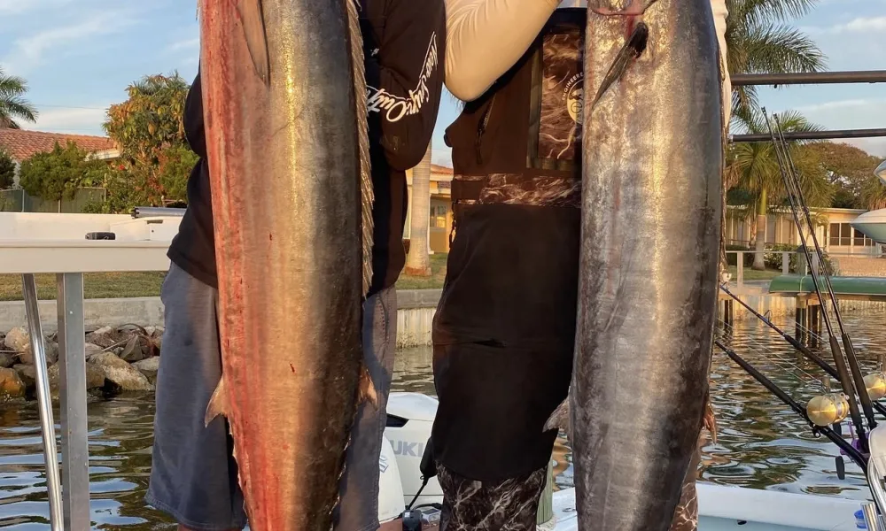 Two anglers holding up wahoo at the dock after an offshore trip with Inverted Fishing Charters